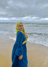 Yezwe modest wear dresses featuring a blue maxi dress with long sleeves and a yellow headscarf by the beach